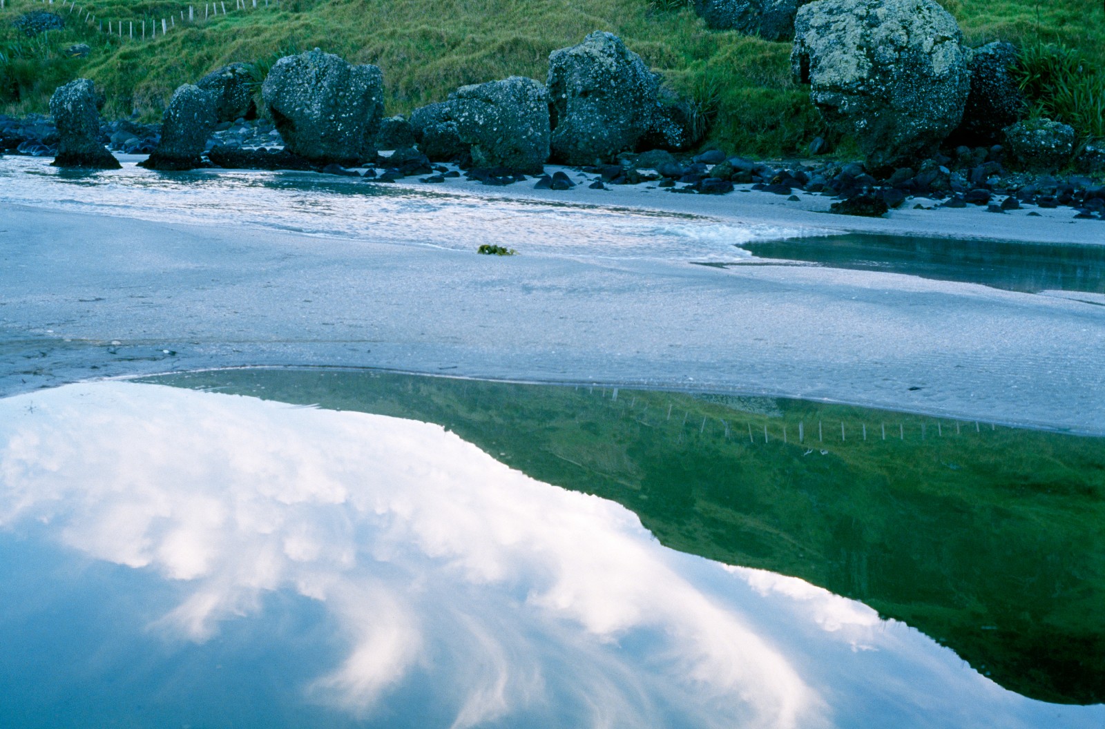 Tohe named this beach Te Horo (walk fast) because of its quicksand; sacred Maori burial ground at Spirits Bay is reflected in the waters of the tidal estuary. At top of picture are work stones which were used by the Maori for shaping tools.