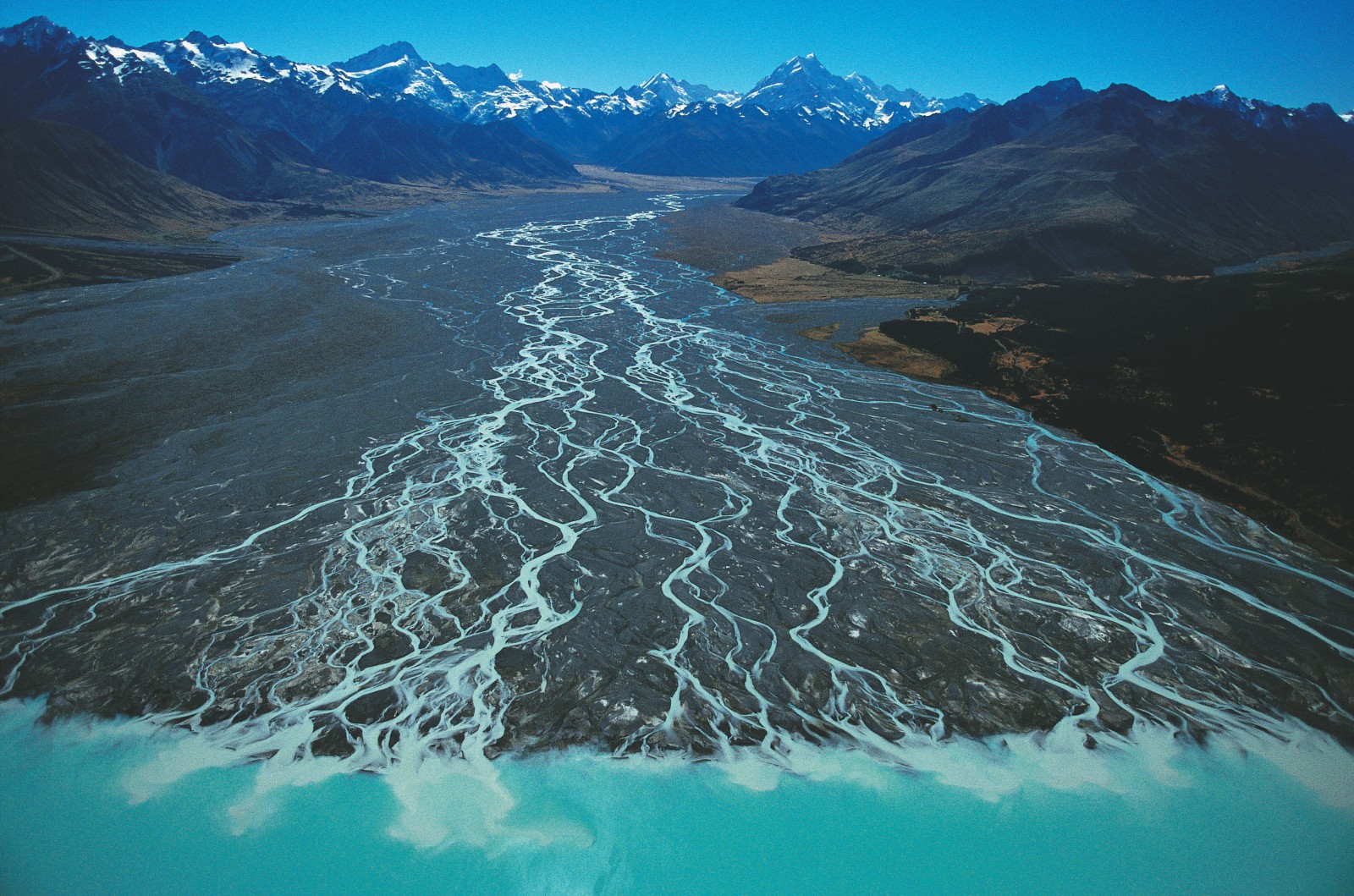41_HighOverNZ_03 Tasman River: A great glacier once carved the broad valley now occupied by the Tasman River, draining into Lake Pukaki, but most of the rock littering the riverbed today has been carried down from much smaller glaciers that remain in the vicinity of Mt Cook-Aoraki--New Zealand's tallest mountain, visible at centre right.